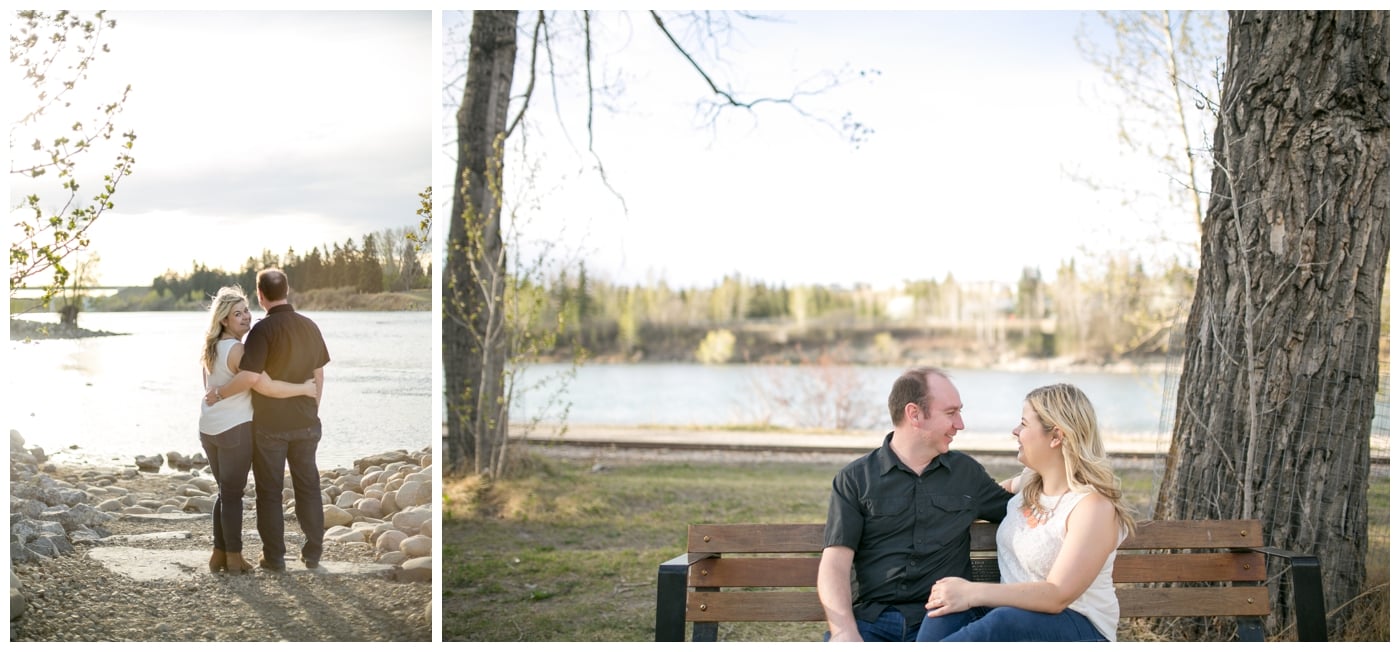 A newly engaged couple sits on a park bench with the Bow RIver behind them at sunset