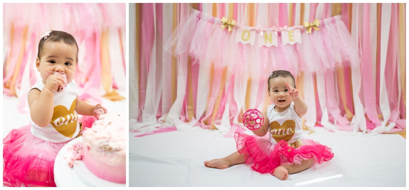 A cake smash shoot of a one-year old Asian girl in a bright pink tulle skirt and a onsie with the word one on it