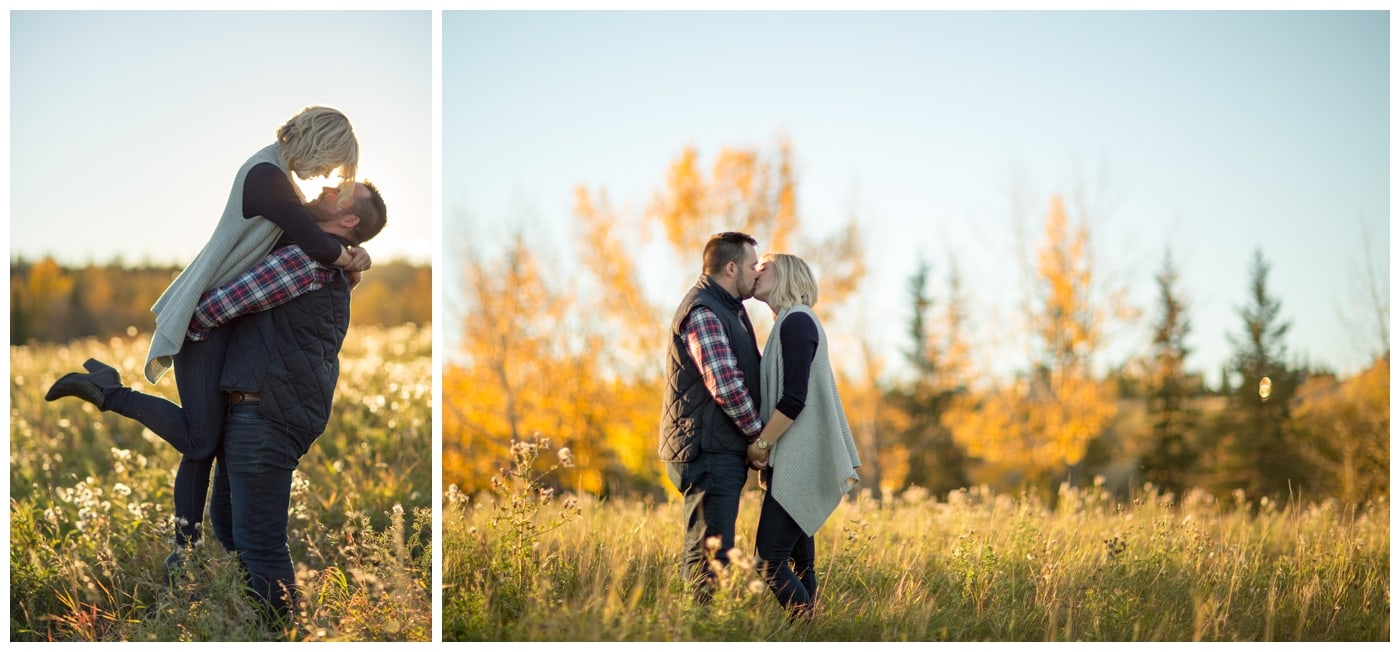 A sunset engagement shoot where the guy is lifting his lady with the sun directly behind them, and kissing in a field with bright yellow autumn trees behind them