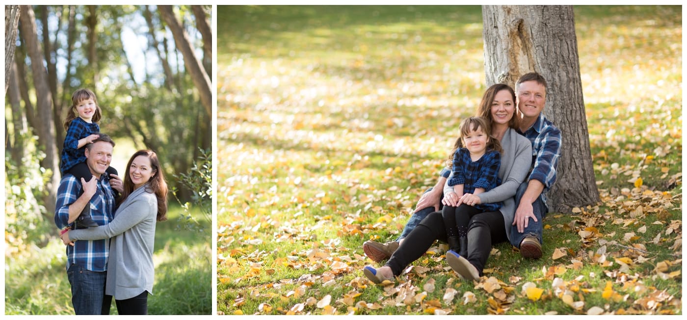 A husband and wife and their young daughter pose in the fall foliage surrounded by trees