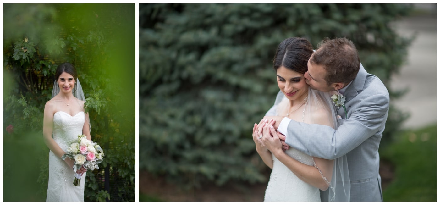 A bride smiles with her bouquet as she is framed by green leaves and kissed gently on the cheek by her husband