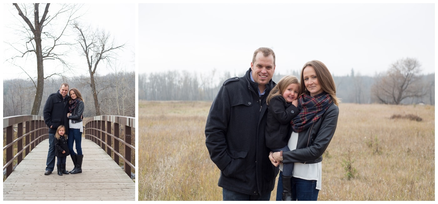 A couple pose with their young daughter on a cold winter day surrounded by trees and yellow grass