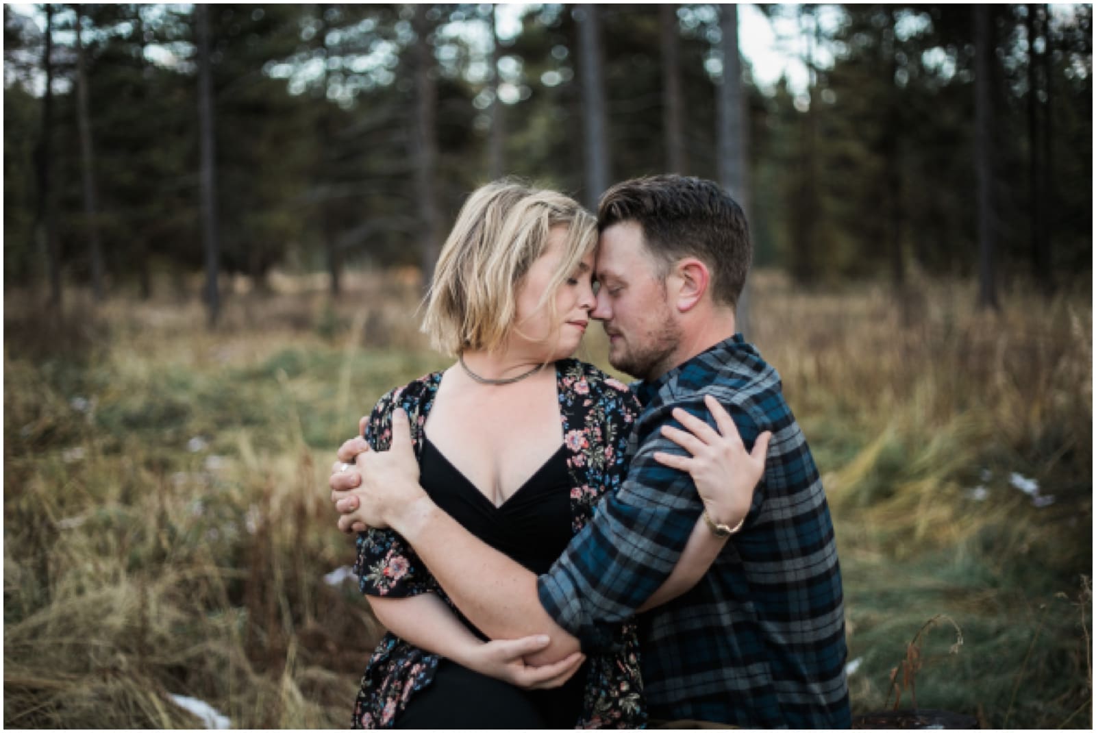 An engaged couple embrase and wrap their arms around each other in a moody wooded area