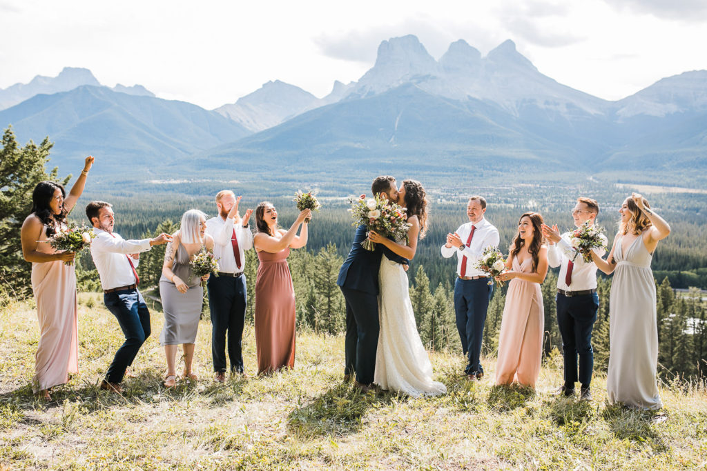 A wedding couple and their bridal party cheer in front of a mountain in Canmore