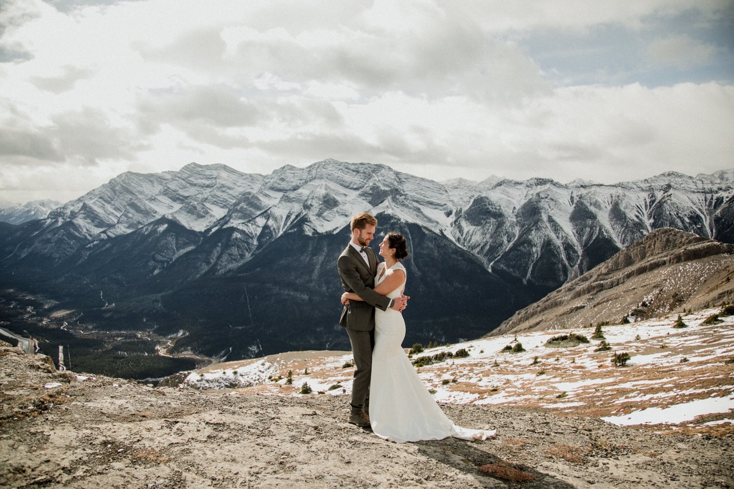 A couple embrassing in a hug on top of a mountain with sweeping mountainviews and clouds in the background