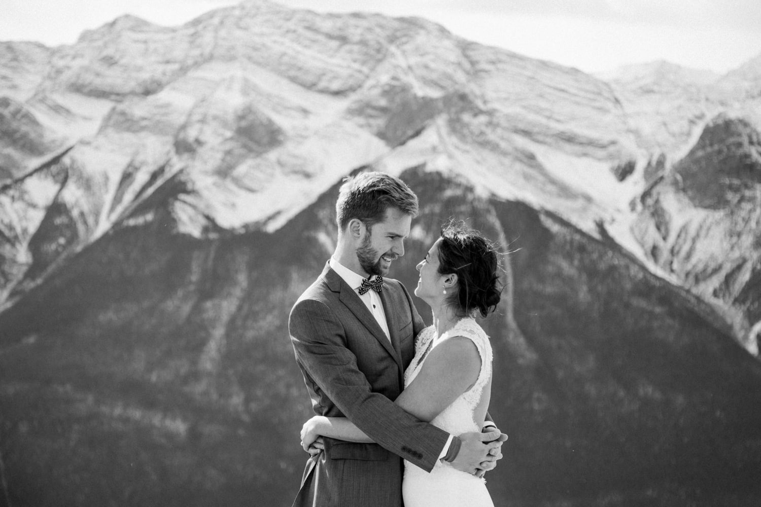 A closeup black and white photo of a couple embrassing with mountain views in the background