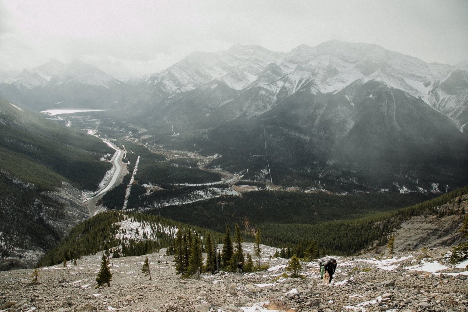 A couple hikes up a mountain with mist and fog in the background making the view of mountains hazy.