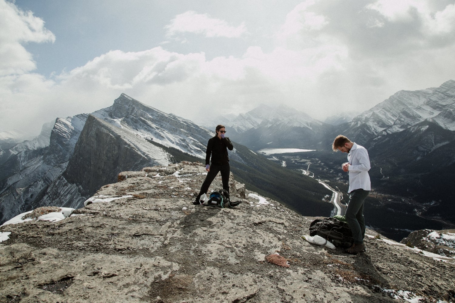 A couple atop a mountain change into wedding attire with view of the Rocky mountains in the background.