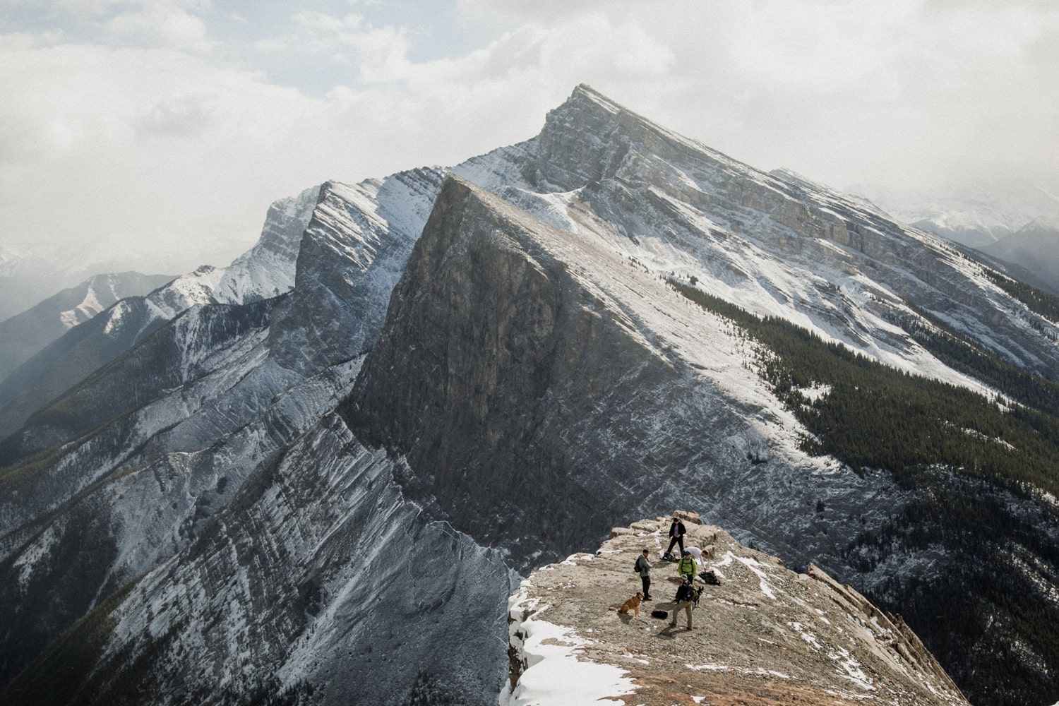 A wide shot of people standing on top of a mountain with Rundle Mountain in Banff in the background