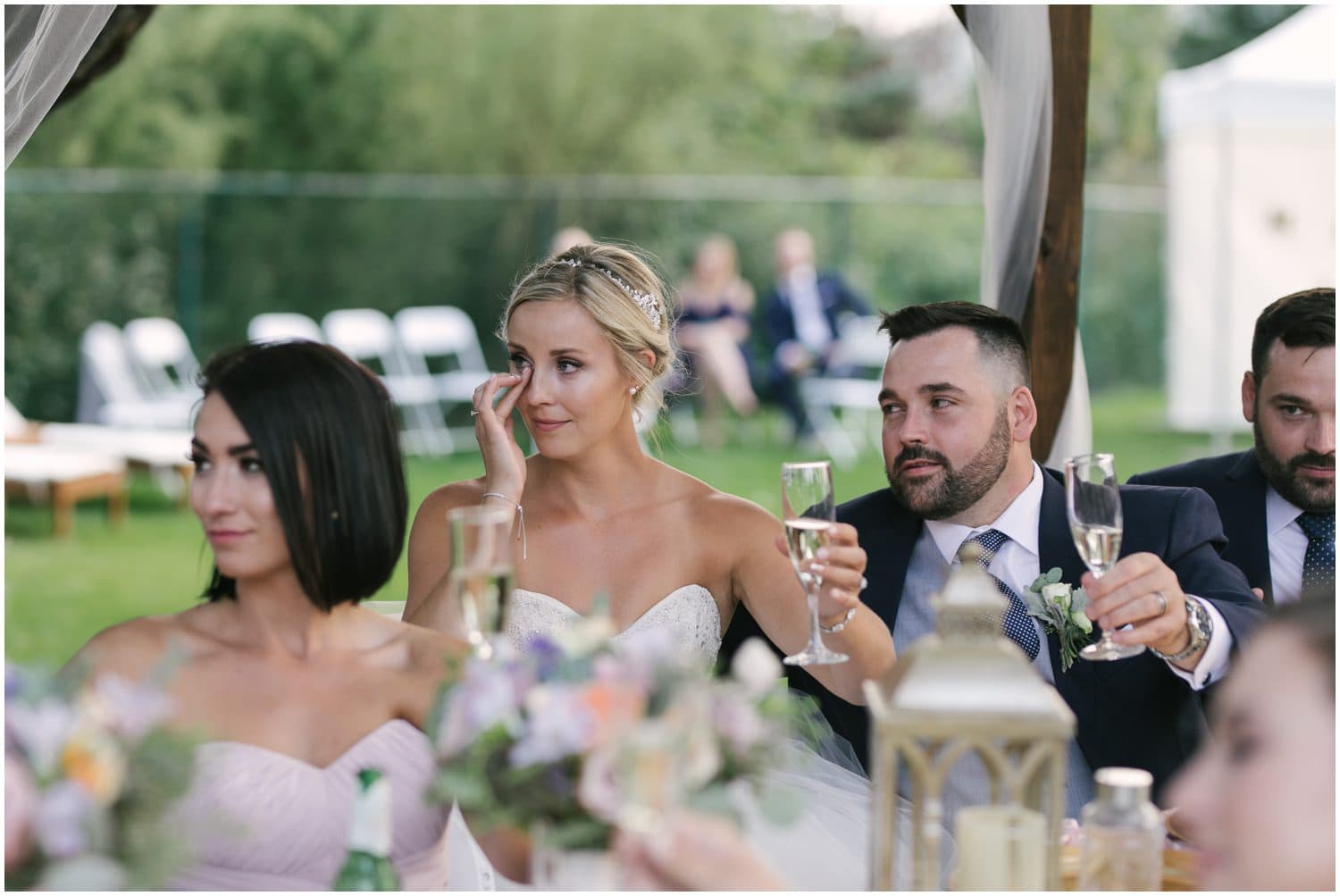 A bride wipes away a tear as she watched a speech being given at her backyard wedding