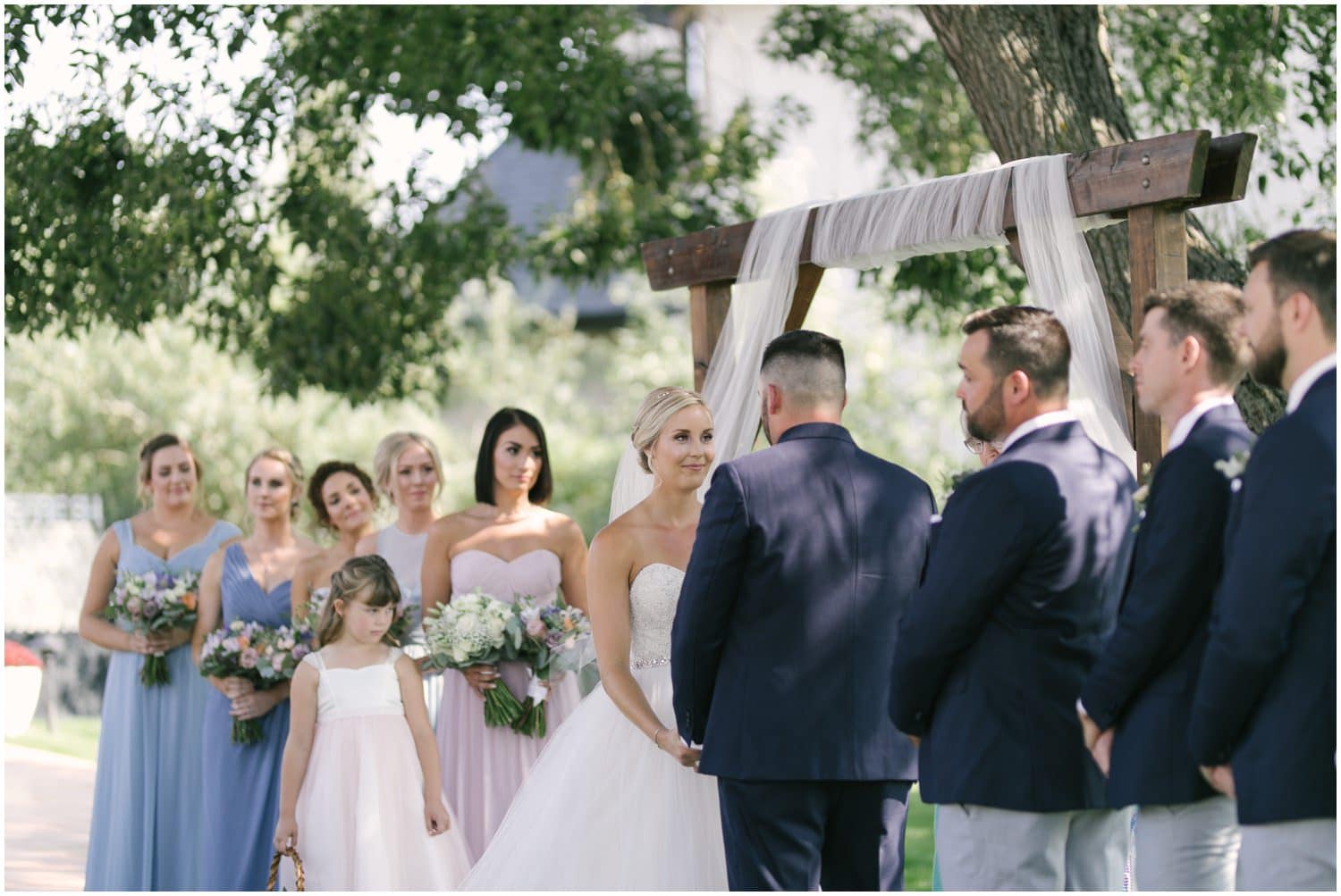 A view of the bride and bridesmaids under a large tree at a wedding in the couple's backyard in Calgary, Alberta. 