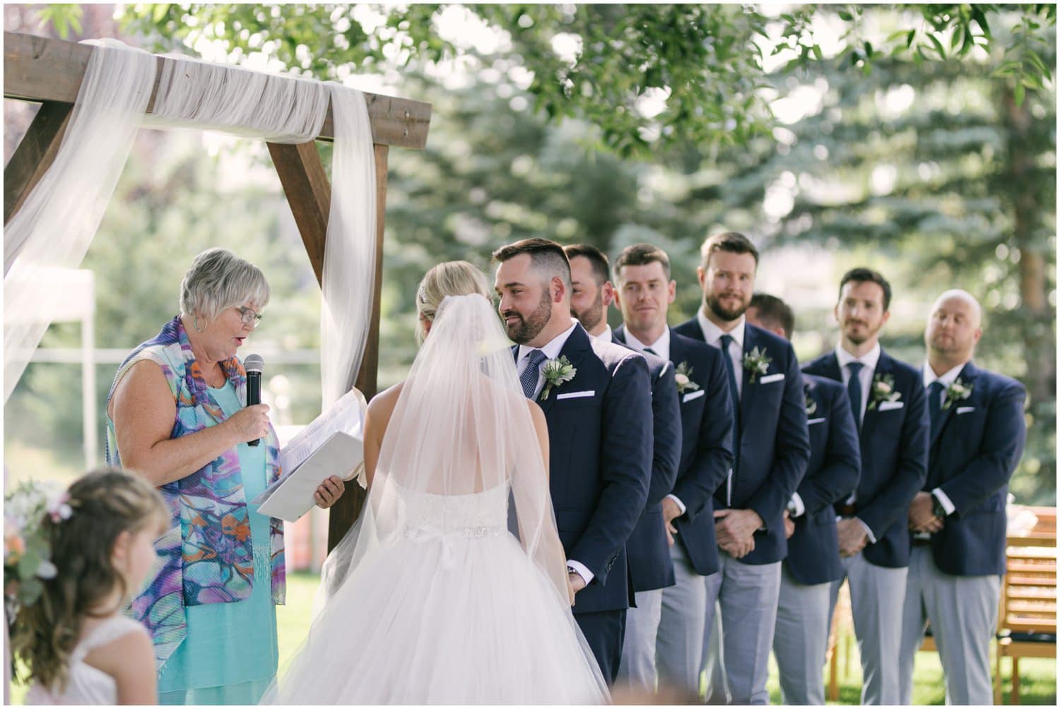 A view of the groom and groomsmen under a large tree at a wedding in the couple's backyard in Calgary, Alberta. 