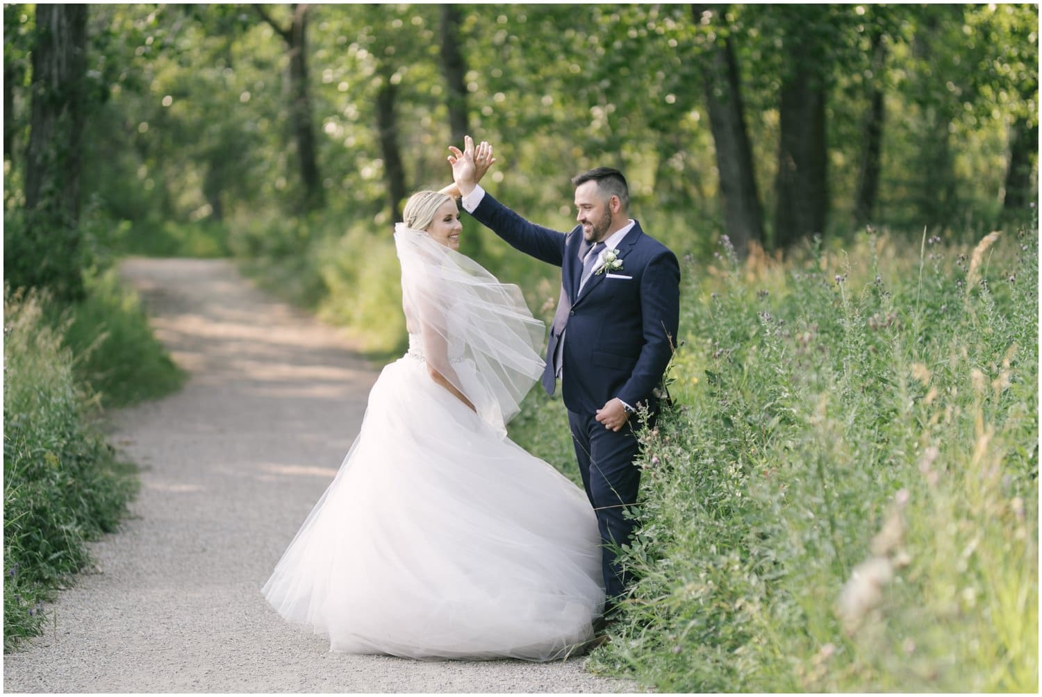 A bride and groom dance in front of beautiful summer green trees in Fish Creek Park in Calgary, Alberta