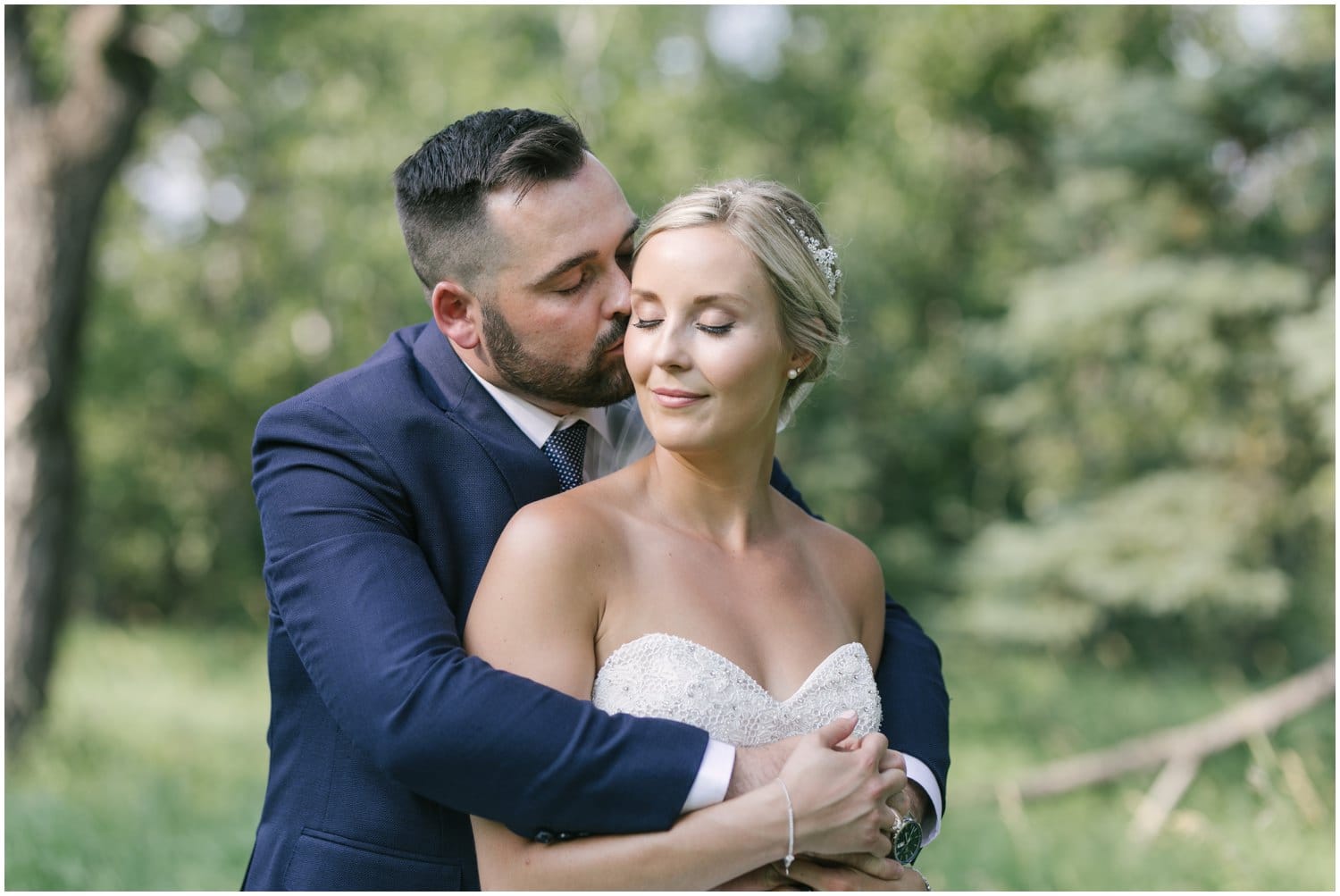 A bride and groom pose in front of beautiful summer green trees in Fish Creek Park in Calgary, Alberta