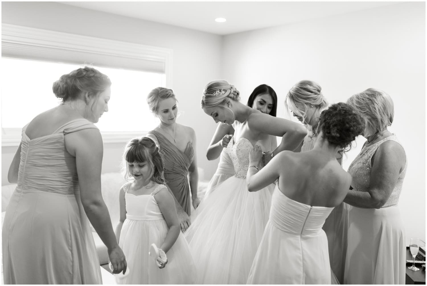 A black and white photo of a bride putting on her dress with her mom and bridesmaids helping