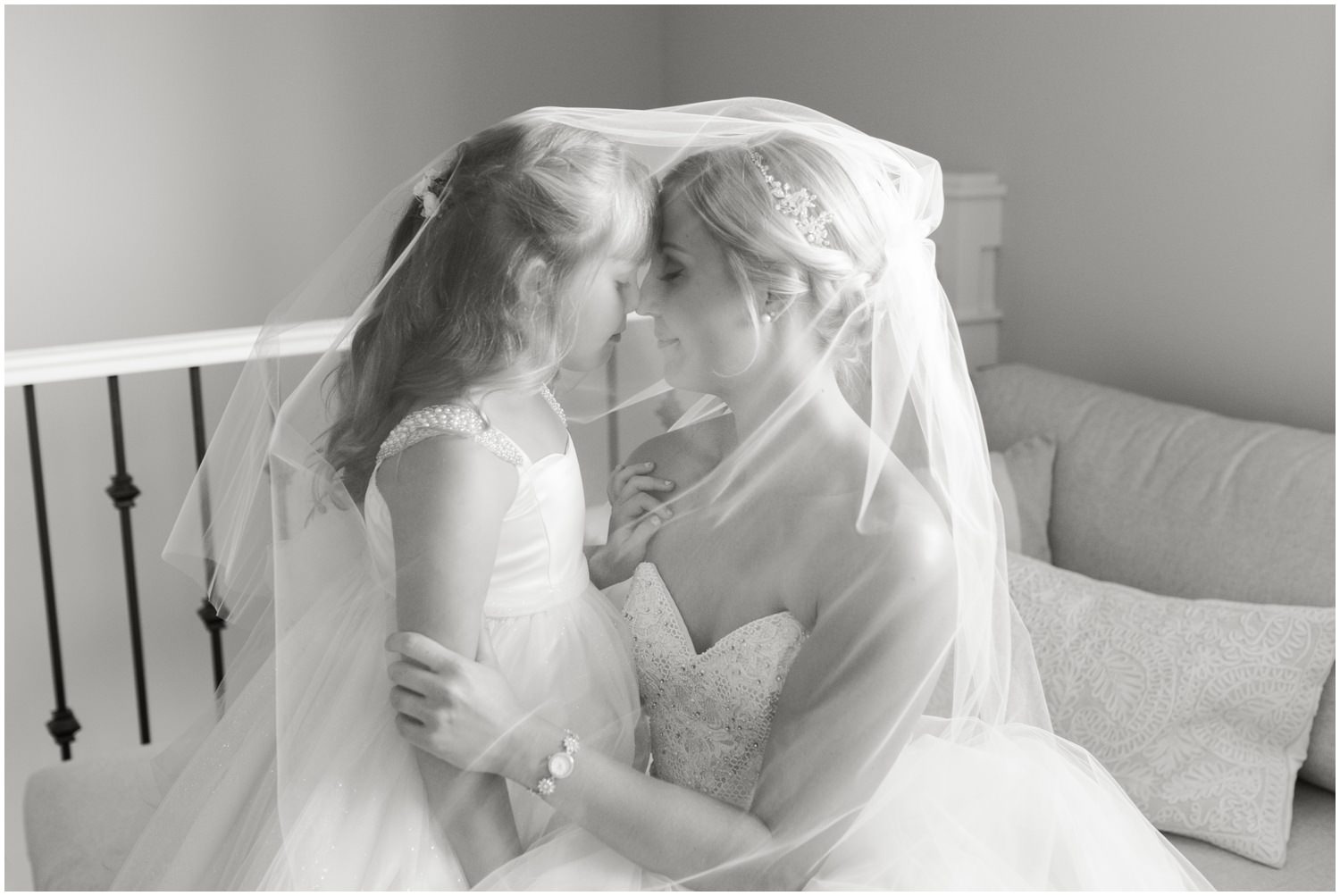 A bride sits facing her young daughter as the are both cloaked by her wedding veil