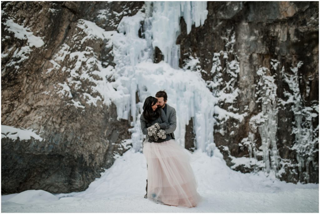 Wedding couple stands in front of a frozen waterfall in the winter