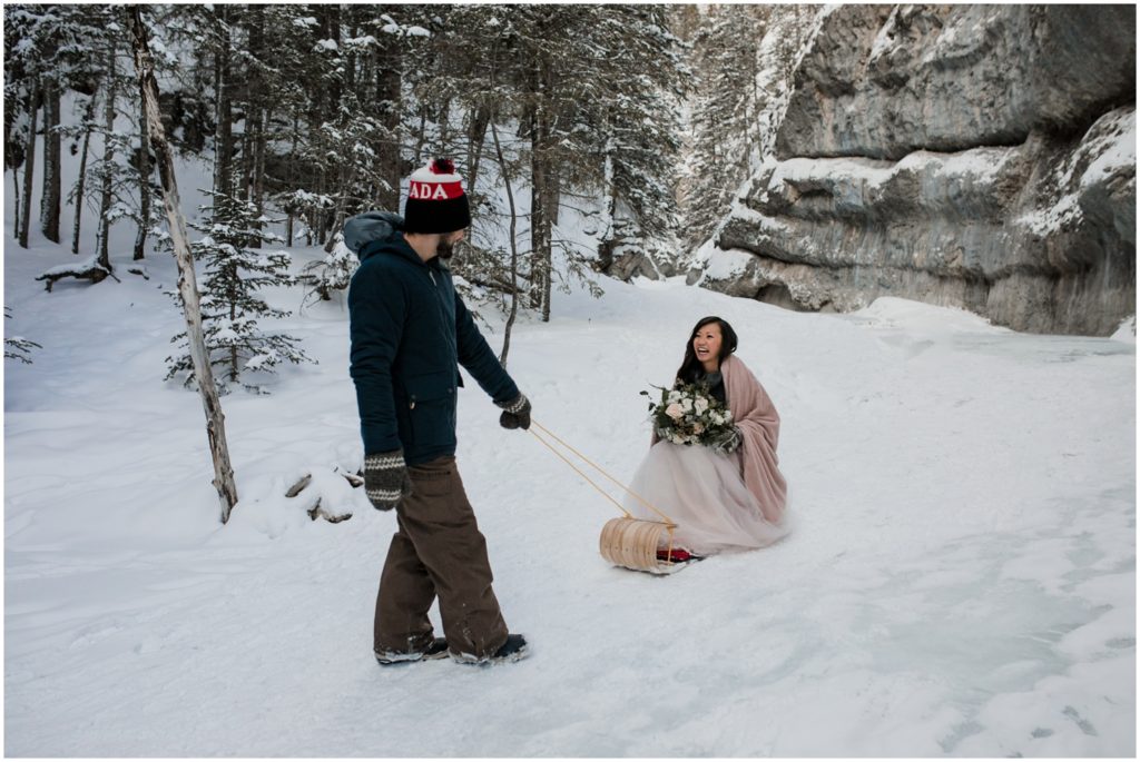 A man pulls his wife across ice on a toboggan during their wedding day