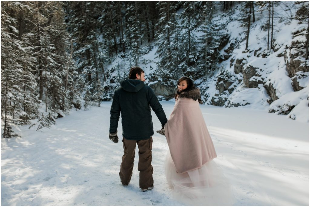 Wedding couple stands in front of a frozen waterfall in the winter