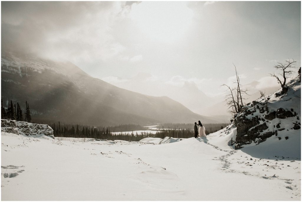 Wedding couple stands in the middle of a snow covered field