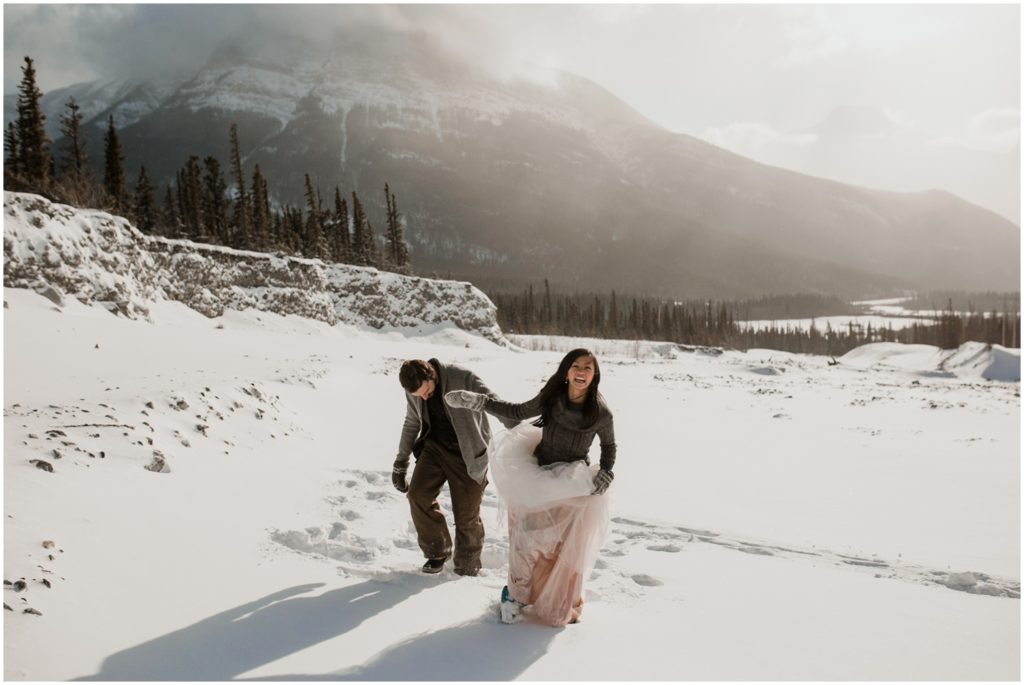 Wedding couple laughs while standing in the middle of a snow covered field