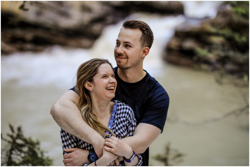 A couple embraces in front of a river at Johnston's Canyon in Banff National Park