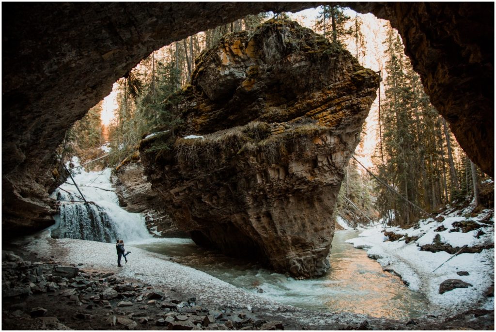 A couple stands in front of the cave and waterfall at Johnston's Canyon in Banff National Park