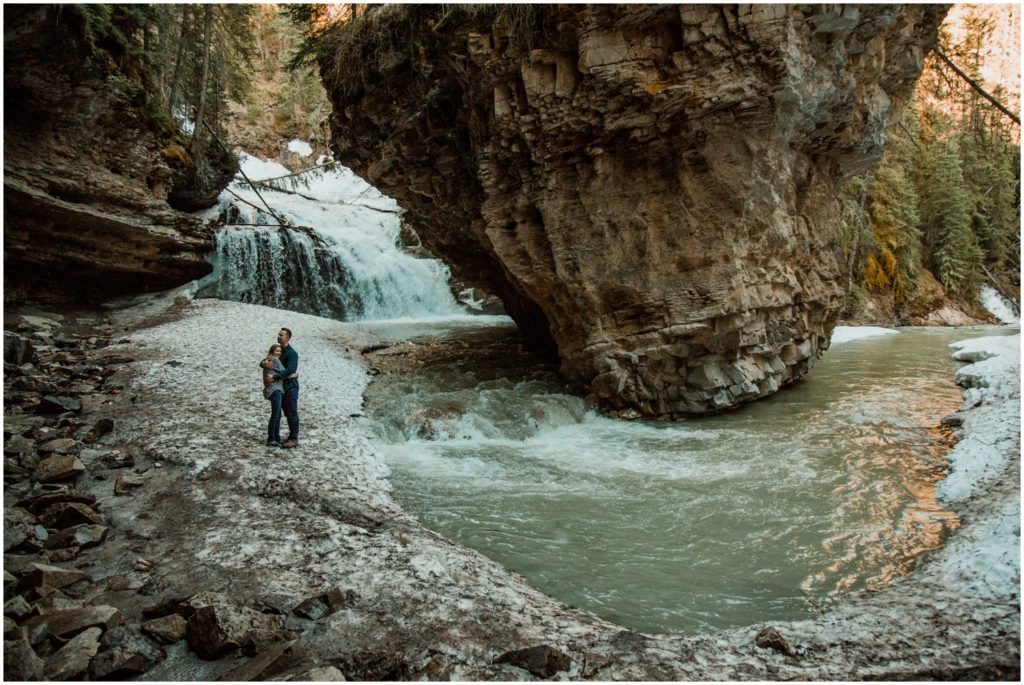 A couple stands in front of the cave and waterfall at Johnston's Canyon in Banff National Park