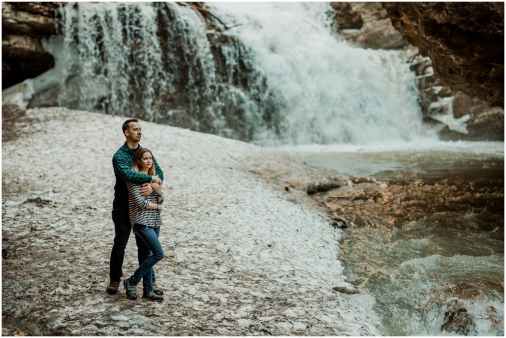 A couple stands in front of the cave and waterfall at Johnston's Canyon in Banff National Park