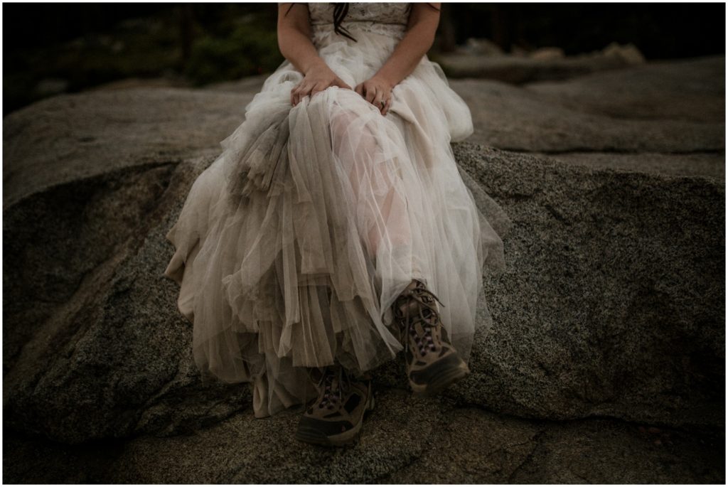 A bride shows her hiking boots and dirty bottom of her dress after a day of adventuring in it