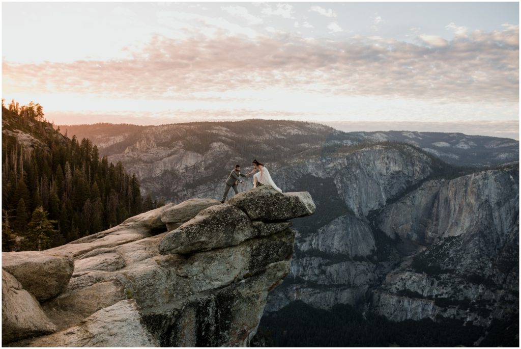 A newly wed couple stands on a ledge during sunset overlooking Yosemite National Park