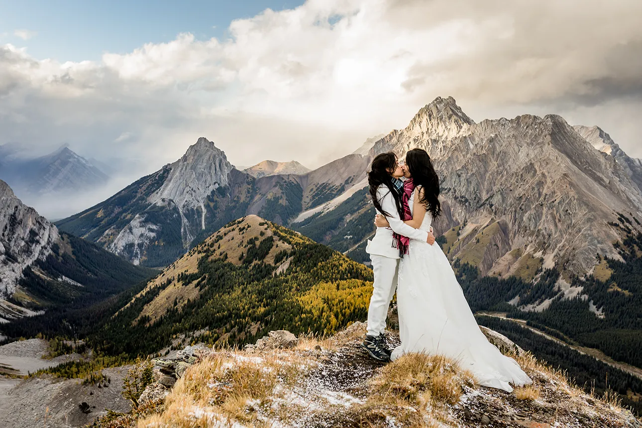 A same sex hiking elopement couple kiss atop a mountaintop in Banff National Park