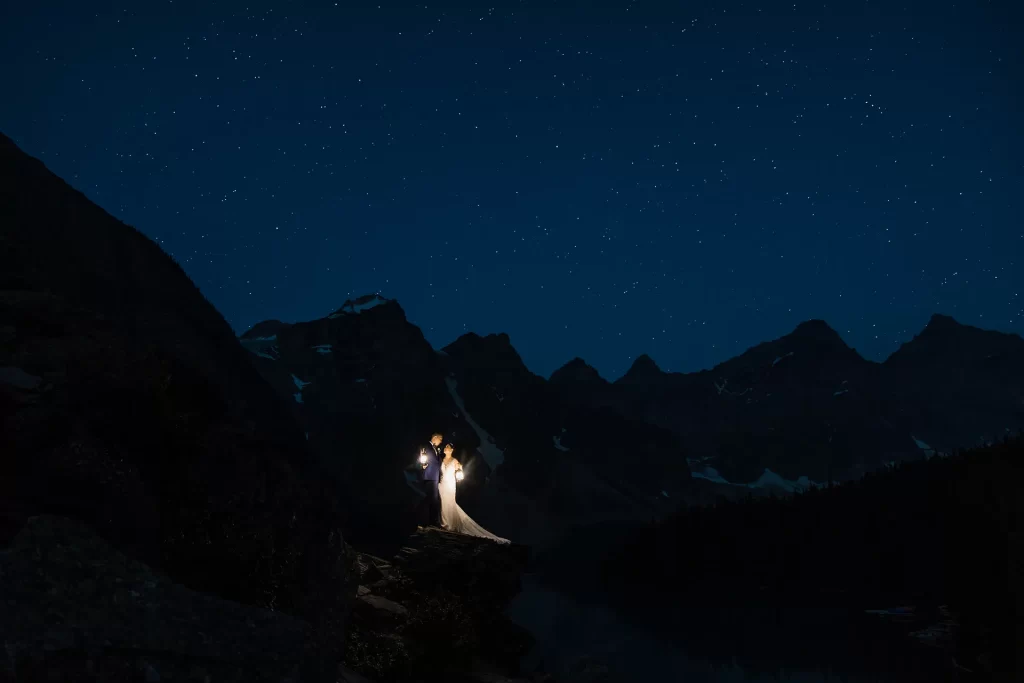 An elopement couple at Moraine Lake stands in the dark under stars holding lanterns