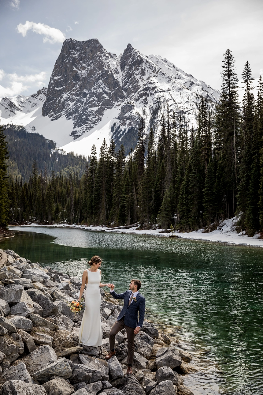 A wedding couple stands on some rocks in front of a mountain at Emerald Lake Lodge