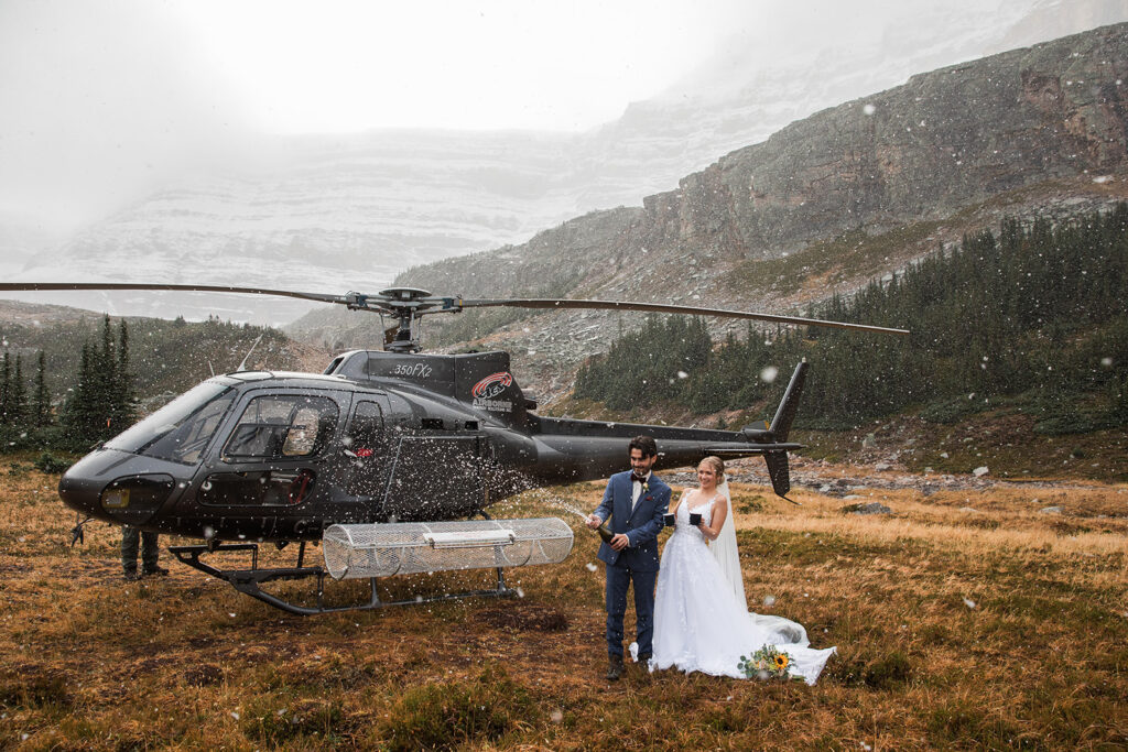 A snowy winter helicopter elopement in Banff surrounded by mountains as the couple pops champagne