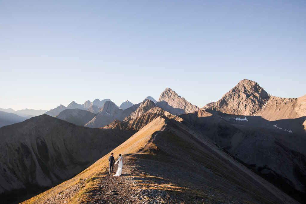 a same sex couple walks hand in hand during their sunrise hiking elopement on tent ridge kananaskis