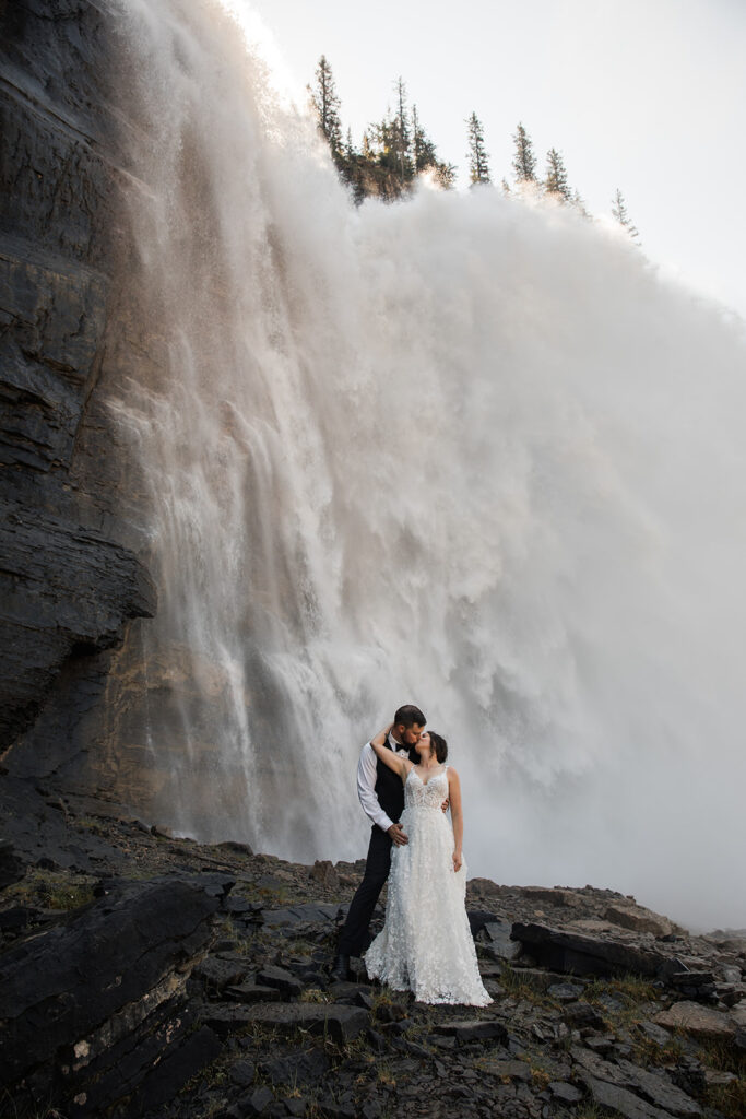 A couple stands in front of Emporer Falls during their adventure elopement at Mount Robson National Park